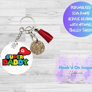 May include: A round white keychain with the words "SUPER DADDY" in colorful letters and a red Mario hat graphic. It includes a gold glitter coin, a red tassel, and the text "PERSONALISED 5CM ROUND ACRYLIC KEYRING WITH OPTIONAL TROLLEY TOKEN."