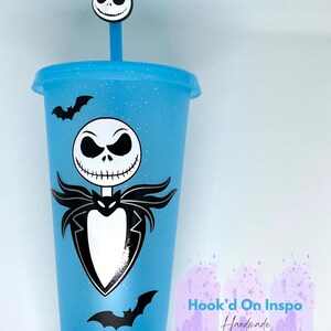 Puede incluir: Un vaso azul claro con tapa y pajita, con un dise&ntilde;o de Jack Skellington y calcoman&iacute;as de murci&eacute;lagos negros. La pajita tiene un dije con la cara de Jack Skellington. El vaso tiene un acabado brillante y el texto "Hook'd On Inspo Handmade With Love".