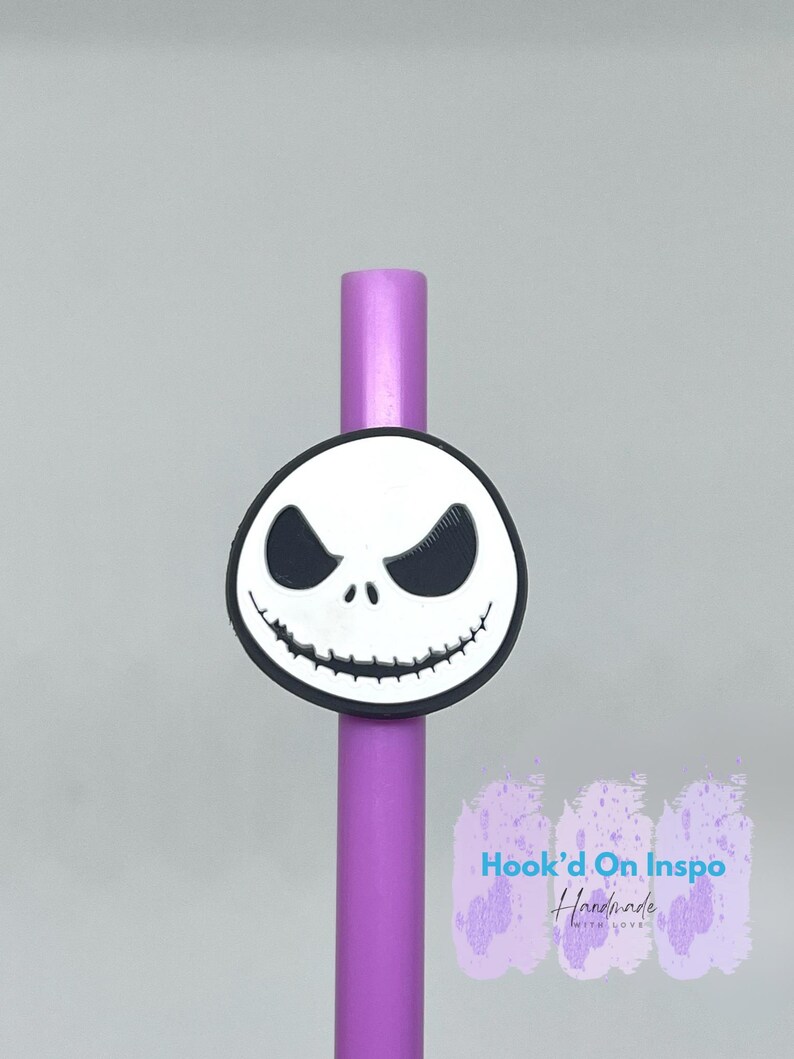 Puede incluir: Una pajita morada con un dije de la cara de Jack Skellington. El dije es blanco con ojos negros y un contorno negro. El texto "Hook'd On Inspo Handmade with love" est&aacute; visible.