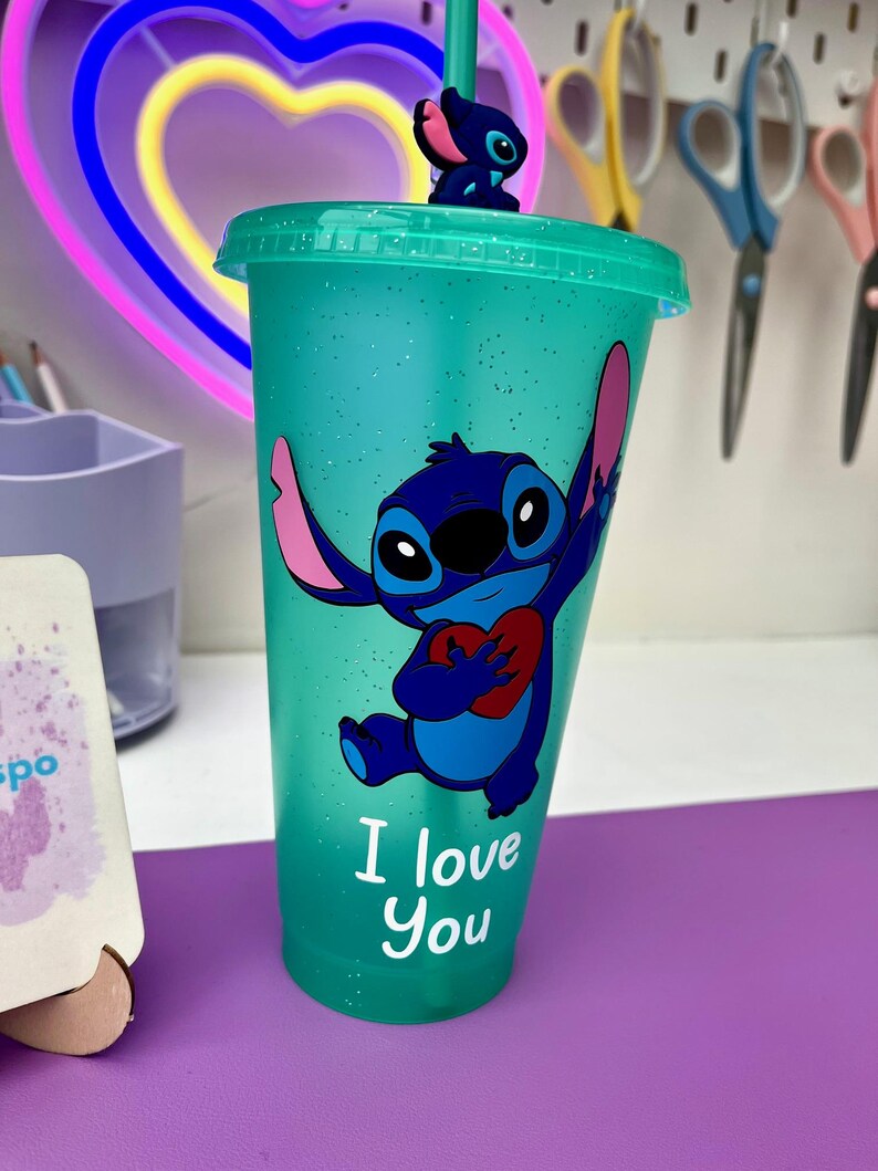 Puede incluir: Un vaso reutilizable azul turquesa con acabado brillante presenta un personaje de dibujos animados azul sosteniendo un coraz&oacute;n rojo. El personaje es Stitch de la pel&iacute;cula de Disney Lilo & Stitch. El texto "I love you" est&aacute; impreso en el vaso.