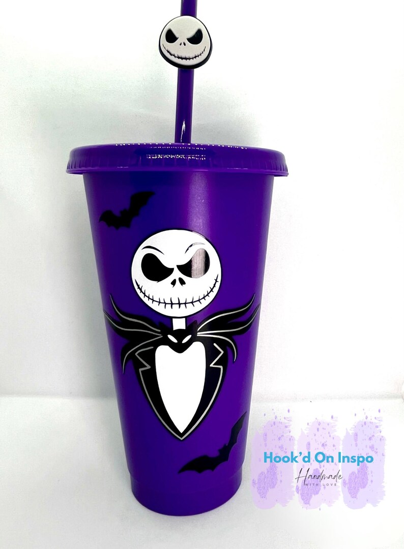 Puede incluir: Un vaso morado con un dise&ntilde;o de Jack Skellington de Pesadilla antes de Navidad. El vaso tiene una tapa y una pajita a juego, rematadas con una cara de Jack Skellington. Tambi&eacute;n hay siluetas de murci&eacute;lagos negros en el vaso.