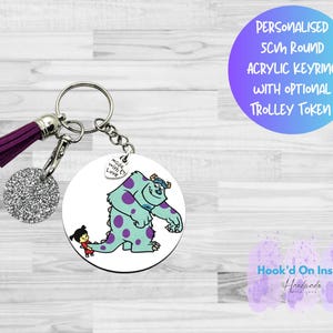 Puede incluir: Un llavero acrílico redondo de 5 cm con una imagen de dibujos animados de Sully y Boo de Monstruos, S.A. El llavero tiene una borla morada y un dije de purpurina plateada. El texto en el llavero dice "PERSONALISED 5CM ROUND ACRYLIC KEYRING WITH OPTIONAL TROLLEY TOKEN."