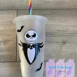 Puede incluir: Un vaso de pl&aacute;stico transparente con tapa y pajita a rayas arco&iacute;ris. El vaso presenta un gr&aacute;fico en blanco y negro de Jack Skellington de Pesadilla antes de Navidad, junto con siluetas de murci&eacute;lagos negros. El texto "Hook'd On Inspo Handmade With Love" es visible.