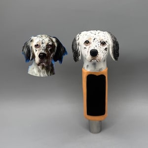 Könnte beinhalten: Eine dekorative Hundekopfskulptur mit schwarzen und weißen Flecken und braunen Augen. Die Skulptur hat eine schwarze rechteckige Form auf orangefarbenem Hintergrund. Ein kleineres Bild eines Hundekopfes befindet sich links.