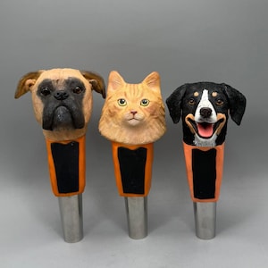 May include: Three decorative bottle stoppers featuring animal faces: a boxer dog, an orange tabby cat, and a black and white dog. Each stopper has an orange and black body and a silver metal base. The dog stoppers have detailed facial features.