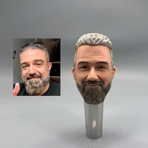 May include: A custom-made bottle stopper featuring a detailed, realistic miniature head of a man with a gray beard and hair. The stopper has a silver-colored base and is a unique, personalized gift.