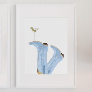 May include: A framed illustration of a pair of light blue cowboy boots with a martini glass resting on top. The martini glass has two green olives in it.