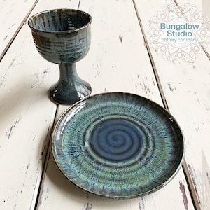 May include: A ceramic chalice and plate set. The chalice has a wide bowl and a pedestal base. The plate is round with a spiral design. Both pieces are glazed in shades of blue and green with a glossy finish.