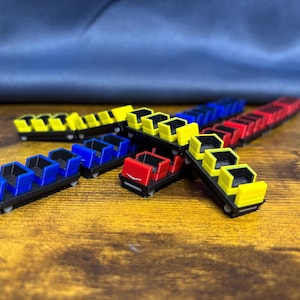 May include: A collection of miniature roller coaster train models in red, blue, and yellow. Each train features multiple open-top passenger cars with black bases and small wheels, arranged in various directions on a wooden surface.