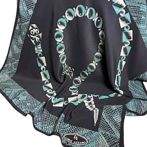 Puede incluir: Un pañuelo azul marino oscuro con un diseño geométrico en color turquesa y blanco. El pañuelo presenta un patrón central similar a un collar y un borde con un diseño de piel de serpiente. La marca "LORIS AZZARO" es visible.