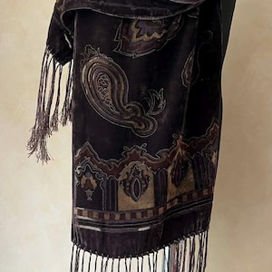 May include: A dark brown velvet scarf with a paisley pattern in shades of brown, gold, and burgundy. The scarf has a fringed edge. The scarf is draped over a mannequin.