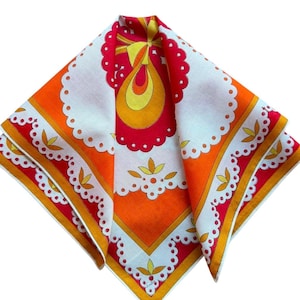 May include: A square scarf featuring a vibrant pattern of orange, red, and yellow hues. The design includes a central stylized motif, scalloped white borders with circular cutouts, and repeating leaf-like shapes arranged in a geometric layout.