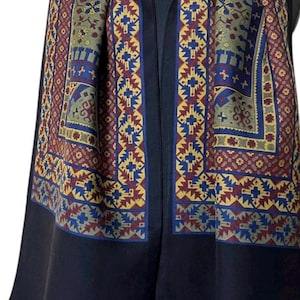 Peut inclure: Une écharpe noire avec une large bordure ornée d'un motif géométrique dans des tons rouge, bleu, jaune et vert olive. L'écharpe présente un panneau central noir uni et des franges noires sur le bord inférieur. Une étiquette blanche indique Seide-Wolle.