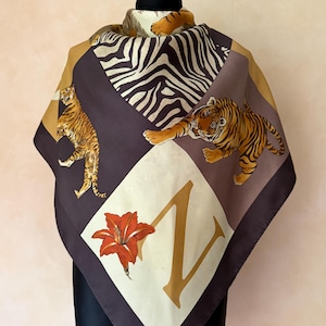 Könnte beinhalten: Ein quadratisches Tuch mit einem Patchwork-Design, das Tiger-Illustrationen, ein Zebramuster und einen großen Buchstaben Z neben einer orangefarbenen Lilienblüte zeigt. Die Farbpalette umfasst Braun-, Beige-, Creme-, Schwarz- und Orangetöne.