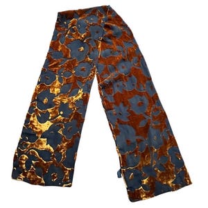 Op de afbeelding: Een lange, rechthoekige sjaal met een bloemenpatroon. De sjaal heeft een donkerblauw bloemmotief tegen een bruine en gouden achtergrond. De sjaal is gemaakt van een zacht, fluwelig materiaal.