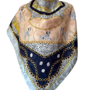 Puede incluir: Un pañuelo cuadrado de seda con una paleta de colores beige y azul marino, con un patrón repetitivo de perros dálmatas, eslabones de cadena dorados y dados blancos. El diseño incluye un fondo con remolinos sutiles y una etiqueta de firma.