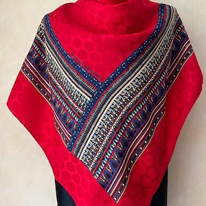 Puede incluir: Un pañuelo de seda rojo vibrante con un diseño de borde geométrico en azul, crema y marrón. El pañuelo presenta el texto "MANOLO BORROMEO" y un patrón de puntos repetidos. Este pañuelo cuadrado se exhibe en un maniquí.