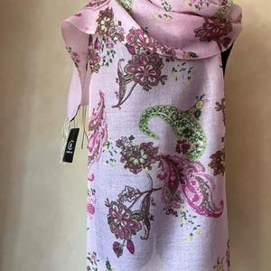 May include: A lilac scarf with a floral paisley pattern. The scarf displays a repeating design of large paisley shapes in pink, green, and brown hues. The scarf is draped over a mannequin, highlighting its length and texture.