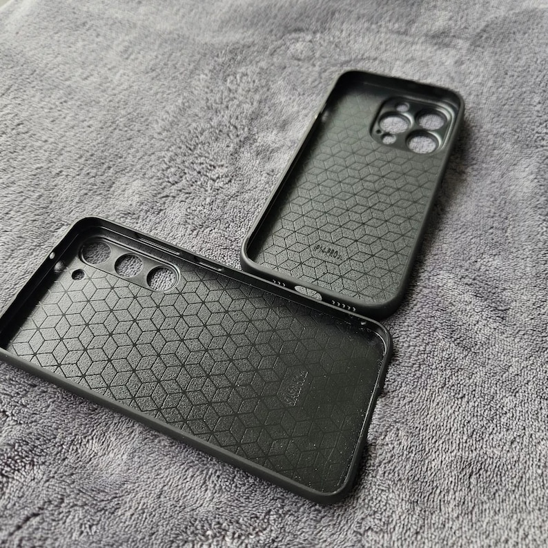 May include: Two black phone cases with a geometric pattern and a raised camera bump. The cases are made of a hard plastic material.