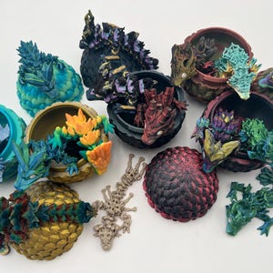 May include: A collection of small, intricately detailed dragon figurines, each perched atop a colorful, textured egg-shaped base. The dragons are painted in various shades of blue, green, red, and black, with intricate details and shimmering scales.