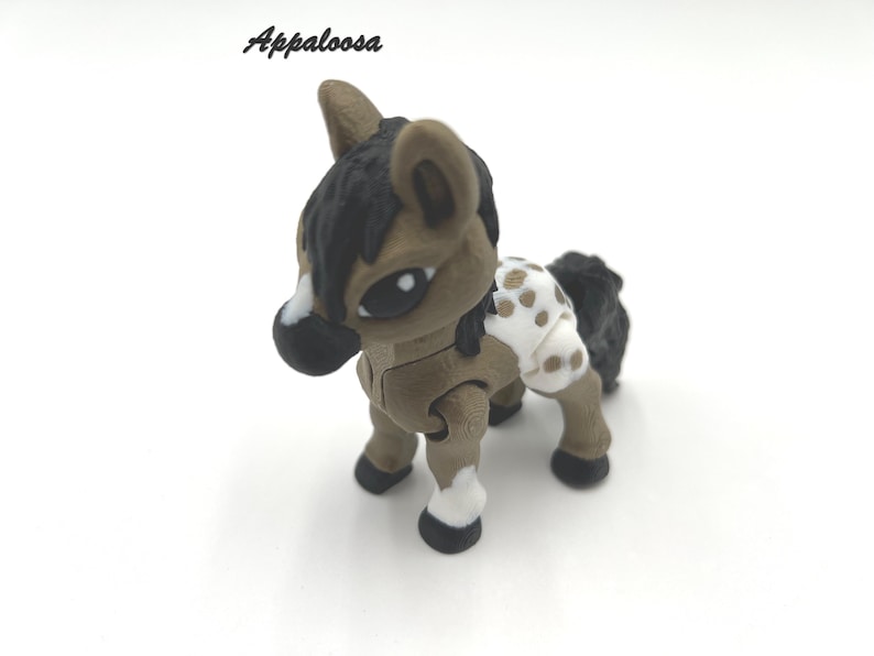May include: A brown and white Appaloosa horse figurine with black hooves and a black mane and tail. The horse has a white saddle blanket with brown spots.