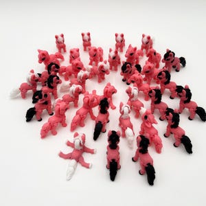 May include: A collection of small, pink pony figurines with black and white manes and tails, arranged in a circular pattern on a white surface. Some ponies are standing, while others are in different poses.