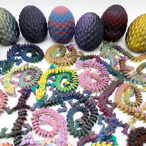 May include: A collection of colorful, 3D-printed dragon eggs and articulated dragons. The eggs are various colors, including purple, gold, and blue, with textured surfaces. The dragons are in various colors and poses.