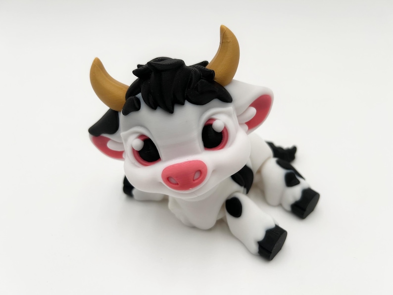 May include: A charming, cartoon-style cow figurine. The cow is primarily white with black spots, black hair, and pink accents on the ears and nose. It has large, expressive eyes and small, yellow horns. The cow is lying down.