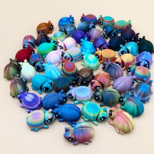 May include: A large collection of small, three-dimensional beetle figurines in a wide variety of colors, including iridescent, metallic, and solid shades. Each beetle features a rounded shell, visible antennae, and dark, prominent eyes.