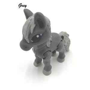 May include: A grey toy horse with a white mane and tail. The horse has articulated legs and a friendly face.