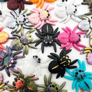 May include: A collection of colorful, handcrafted spider figurines in various colors, including black, pink, white, and blue. Each spider has detailed features and a unique design, perfect for Halloween decorations or craft projects.