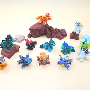 May include: A collection of small, multi-colored dragon figurines in various poses, including some perched on brown rock-like structures. The dragons feature vibrant colors such as orange, green, blue, black, and white with detailed scales and wings.