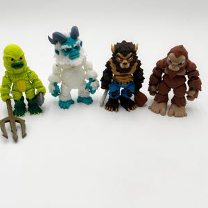 May include: Four articulated monster action figures standing in a row. The first is a lime green aquatic creature with a trident, the second is a white and blue yeti, the third is a brown werewolf in blue pants, and the fourth is a brown ape-like creature.