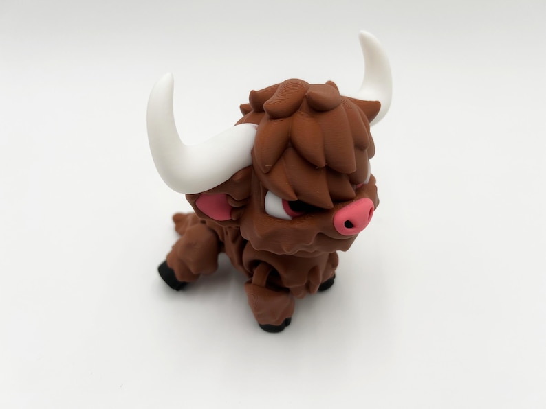 May include: A brown figurine of a Highland cow with white horns, pink inner ears, and a pink nose. The cow has a shaggy coat and black hooves. The figurine is on a white background.