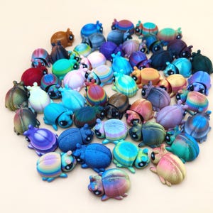 May include: A large collection of small, three-dimensional beetle figurines in a wide variety of colors, including iridescent, metallic, and solid shades. Each beetle features a rounded shell, visible antennae, and two dark, prominent eyes.