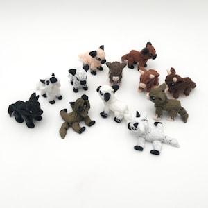 May include: A collection of small, handmade animal figurines in various colors, including black, white, brown, and tan. The figurines appear to be crafted from a soft, textured material, and are arranged on a white surface.