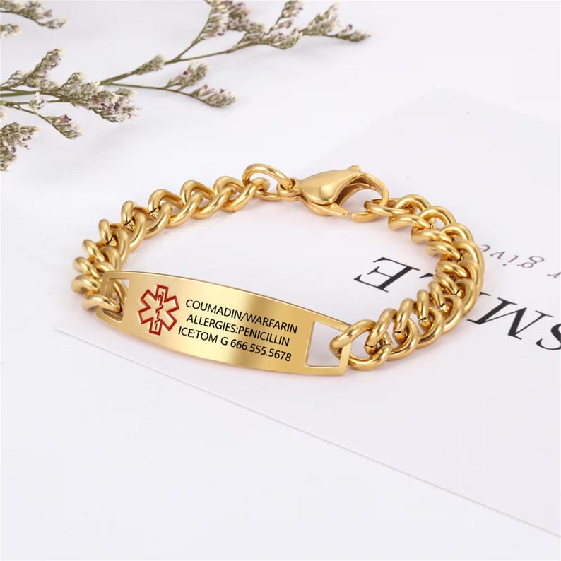 May include: Gold-colored medical ID bracelet with a curb chain design. The rectangular ID plate features a red medical symbol and printed text: COUMADIN/WARFARIN, ALLERGIES: PENICILLIN, ICE: TOM G 666.555.5678. The bracelet has a lobster clasp.