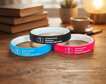 Op de afbeelding: Drie siliconen medische alarmarmbanden in zwart, blauw en roze, elk met een witte binnenkant. Elke band is voorzien van een wit Ster van het Leven-symbool, de tekst Justice ward Seizyure en de contactgegevens ICE:903-285-4631 in witte opdruk.