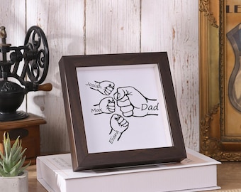 May include: A brown framed picture with a white background and black silhouette of five fists with the names Josiah, Max, Eliana, and Dad written on them.