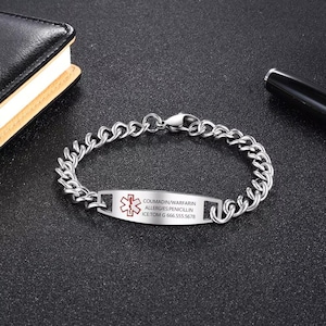 May include: A silver-colored medical ID bracelet with a chain link design. The rectangular plate displays a red medical symbol and text: COUMADIN/WARFARIN, ALLERGIES: PENICILLIN, ICE: TOM G 666.555.5678. The bracelet is on a dark surface.