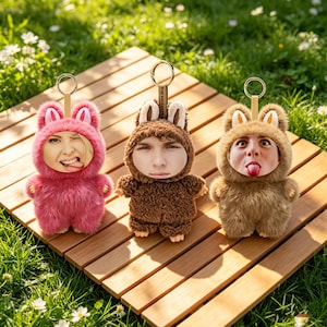 May include: Three plush keychains in the shape of bunnies, each with a different face. The keychains are in pink, brown, and tan. Each keychain has a gold-colored ring and a small leather strap. The keychains are on a wooden surface.