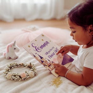 May include: A child reads a book with the name "Emma" and the text "Will you be my Flower Girl?" on the cover. A plush unicorn, a floral crown, and a pink tutu are also visible. The book features a castle illustration.