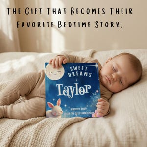 May include: A sleeping baby lies on a bed, holding a blue book titled "Sweet Dreams Taylor." The book features a moon and a bunny illustration. The text above reads, "THE GIFT THAT BECOMES THEIR FAVORITE BEDTIME STORY."