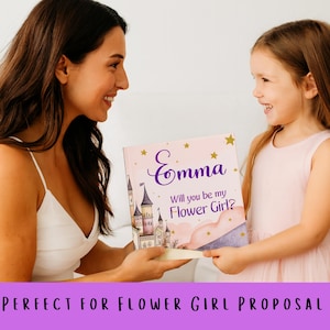 May include: A pink book with the name "Emma" in purple script and the text "Will you be my Flower Girl?" is held by two people. The book features a castle illustration and gold stars. The book is a flower girl proposal gift.