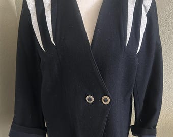 May include: Black wool blazer with a V-neck and double-breasted closure. The blazer features gray and white striped accents on the shoulders and two decorative buttons. The sleeves are cuffed, revealing a navy blue lining.