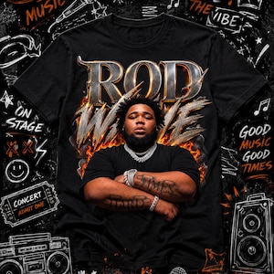 May include: A black t-shirt featuring a graphic of Rod Wave with the text "ROD WAVE" in metallic lettering above him, surrounded by flames. The design includes white line art of a microphone, a boombox, a speaker, and text like "LIVE MUSIC".