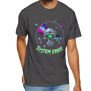 May include: Dark grey t-shirt with a graphic design. The design features a skull with a neon green eye, and the text "SYSTEM ERROR." The design includes a circular element with purple, green, and blue hues, and smaller skulls on each side.