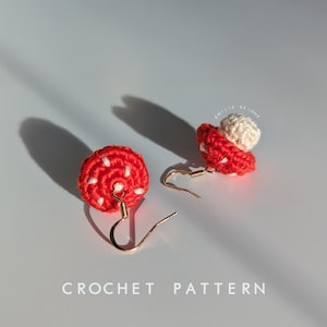 May include: A pair of crocheted mushroom earrings with red caps and white spots, and white stems. The earrings are attached to gold hooks.