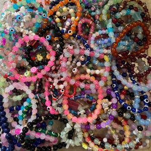May include: A large pile of colorful beaded bracelets with various charms, including evil eye beads, fruit charms, and gemstone beads.