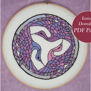 May include: A cross-stitch pattern featuring three purple and pink cranes in a circular design. The pattern is in a wooden embroidery hoop and is ready for instant download as a PDF.